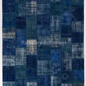 Pode incluir: Um tapete de patchwork com um esquema de cores azul e branco. O tapete é feito de diferentes pedaços de tecido costurados juntos para criar um design único. O tapete é de forma retangular e tem uma borda franjada.