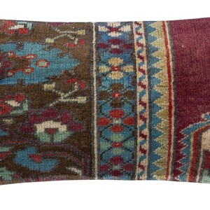 Puede incluir: Cojín decorativo rectangular con diseño de alfombra vintage. El cojín presenta una paleta de colores marrón, turquesa y burdeos con patrones florales y geométricos. El cojín tiene un aspecto suave y texturizado.