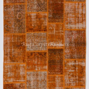 May include: A patchwork rug with a variety of orange and brown tones. The rug is made up of many different pieces of fabric that have been sewn together. The rug has a distressed look and is perfect for adding a touch of vintage style to any room.