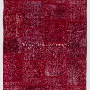 May include: A red patchwork rug with a variety of textures and patterns. The rug is made up of many small squares sewn together.