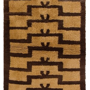 May include: A brown and beige geometric patterned rug with a fringe border. The rug has a modern design with a repeating pattern of squares and rectangles.