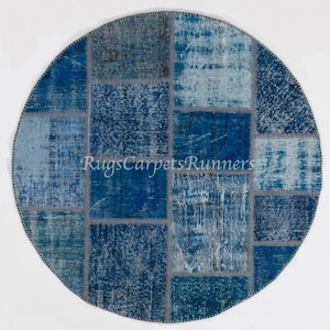 Può includere: Tappeto rotondo in patchwork di colore blu e bianco. Il tappeto è realizzato con diversi pezzi di tessuto cuciti insieme. Il tappeto ha un aspetto vissuto ed è perfetto per aggiungere un tocco di stile bohémien a qualsiasi stanza.
