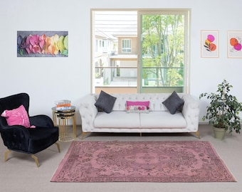 May include: A living room with a pink patterned rug, a white tufted sofa with grey cushions, and a black armchair with a pink cushion. Artwork and a small side table are also present.