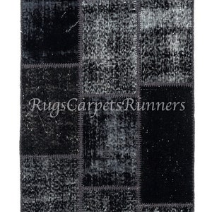 Pode incluir: Um tapete de patchwork preto e branco com um visual desgastado. O tapete é feito de diferentes pedaços de tecido costurados juntos. O tapete tem uma forma retangular e mede aproximadamente 60 cm de largura e 180 cm de comprimento.