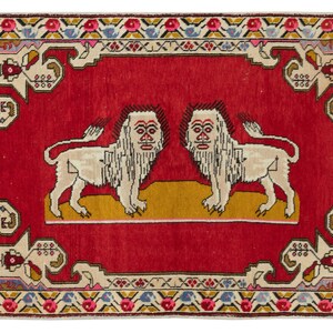 May include: A red rectangular rug with a central design of two stylized lions facing each other. The lions are white with detailed manes and stand on a yellow base. The rug has a decorative border with floral and geometric patterns.