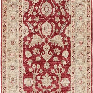 May include: A rectangular area rug featuring a deep red central field adorned with intricate beige floral and vine motifs. The rug is framed by a wide, light beige border decorated with repeating floral patterns in red and tan, with fringed edges.