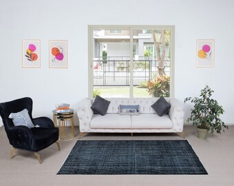 Könnte beinhalten: Ein weißes Sofa mit gesteppter Polsterung und goldenen Beinen steht in einem Wohnzimmer mit einem blauen Teppich, zwei schwarzen Sesseln und einem Satz von drei goldenen Nisttischen. Zwei gerahmte abstrakte Bilder mit rosa und orangefarbenen Kreisen hängen an der Wand.