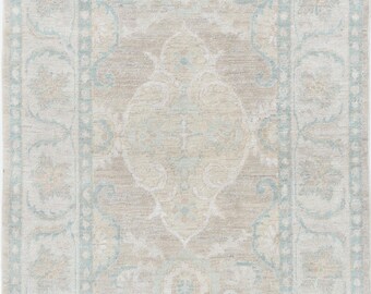 Puede incluir: Una alfombra rectangular que presenta un medallón central y un borde ancho con intrincados patrones florales y de enredaderas. La paleta de colores consiste en tonos beige suave, crema y azul claro apagado, creando un diseño equilibrado.