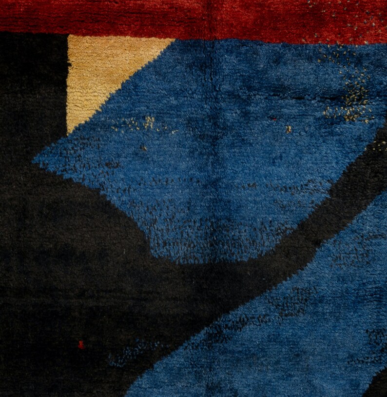 May include: Close-up of a blue, black, and beige rug with an abstract geometric pattern. The rug has a textured, woven surface.