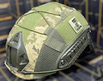 May include: A green and brown camouflage helmet with a black patch that says "FOR THE PEOPLE" and a trident symbol. The helmet has a mesh panel and a black strap.