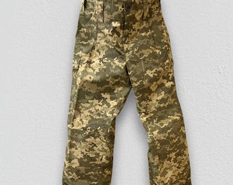 May include: A pair of pants featuring a digital camouflage pattern in shades of olive green, tan, and brown. The pants have a structured waistband with a button closure, belt loops, and side cargo pockets on the thighs with a straight leg cut.