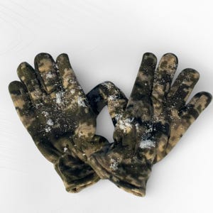 May include: A pair of camouflage gloves, featuring a pattern of green, brown, and tan hues. The gloves are shown on a white background and appear to have a light dusting of snow or a similar substance on them.