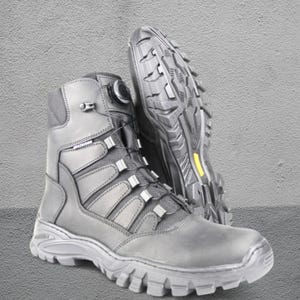 May include: Black tactical boots with a high-top design. The boots feature a lace-up system with a dial, reinforced panels, and a rugged outsole. The sole has a yellow accent. The boots are designed for durability and support.