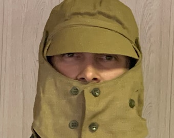 May include: A tan-colored winter hat with a fold-down flap that covers the face. The hat has a visor and multiple buttons.
