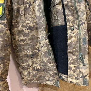 May include: A camouflage jacket with a zipper closure and a patch featuring the Ukrainian trident symbol on the left sleeve.