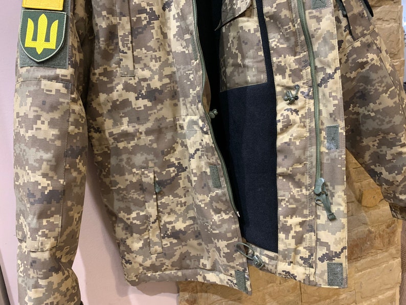 May include: A camouflage jacket with a zipper closure and a patch featuring the Ukrainian trident symbol on the left sleeve.
