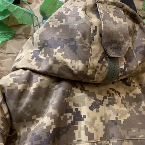 May include: A camouflage jacket with a hood and a zipper closure. The jacket is made of a durable, water-resistant fabric and features a variety of pockets.