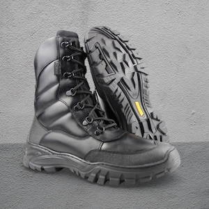 Puede incluir: Botas de combate de cuero negro con suela robusta. Las botas tienen un diseño con cordones con ojales metálicos y un cuello acolchado. La suela es gruesa y texturizada para el agarre. Una bota está en posición vertical, la otra inclinada.