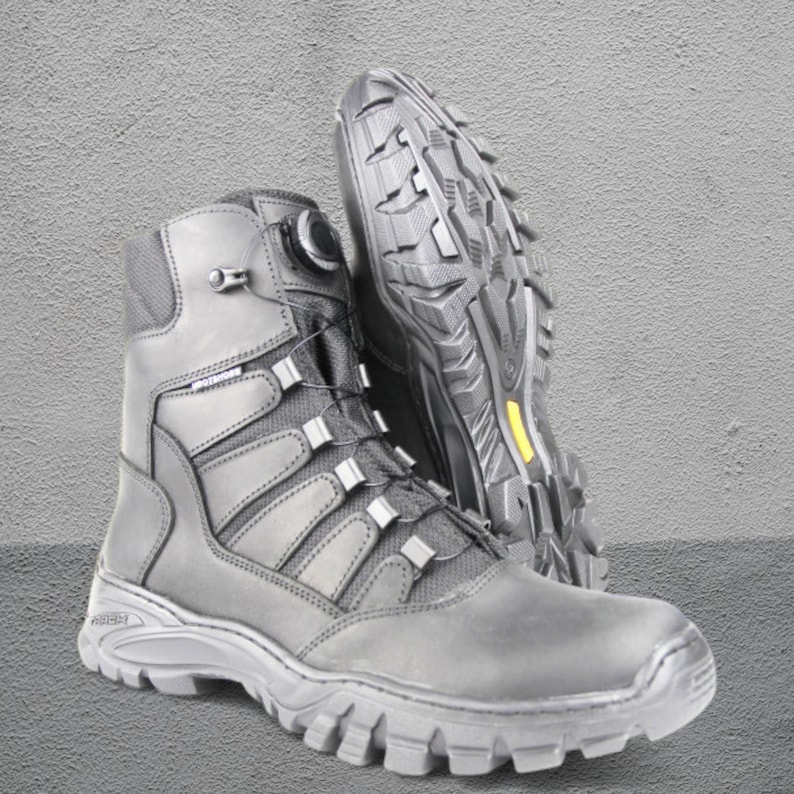 May include: Black tactical boots with a high-top design. The boots feature a lace-up system with a dial, reinforced panels, and a rugged outsole. The sole has a yellow accent. The boots are designed for durability and support.