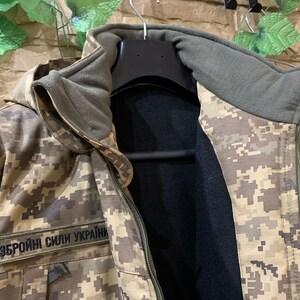 May include: A camouflage jacket with a black fleece lining and a zipper closure. The jacket has a hood and a patch that reads "Збройні Сили України".