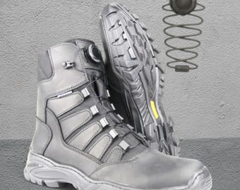 May include: Gray tactical boots with a rugged sole and a unique lacing system. The boots have a high-top design and are made of durable materials. The soles are thick and provide excellent traction. A yellow accent is visible on the sole.