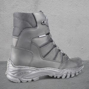 May include: A gray tactical boot with a high-top design. The boot features a lace-up closure, a padded collar, and a rugged sole. The word "TREK" is visible on the sole. The boot is made of durable materials and is suitable for outdoor activities.