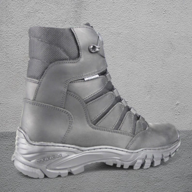 May include: A gray tactical boot with a high-top design. The boot features a lace-up closure, a padded collar, and a rugged sole. The word "TREK" is visible on the sole. The boot is made of durable materials and is suitable for outdoor activities.