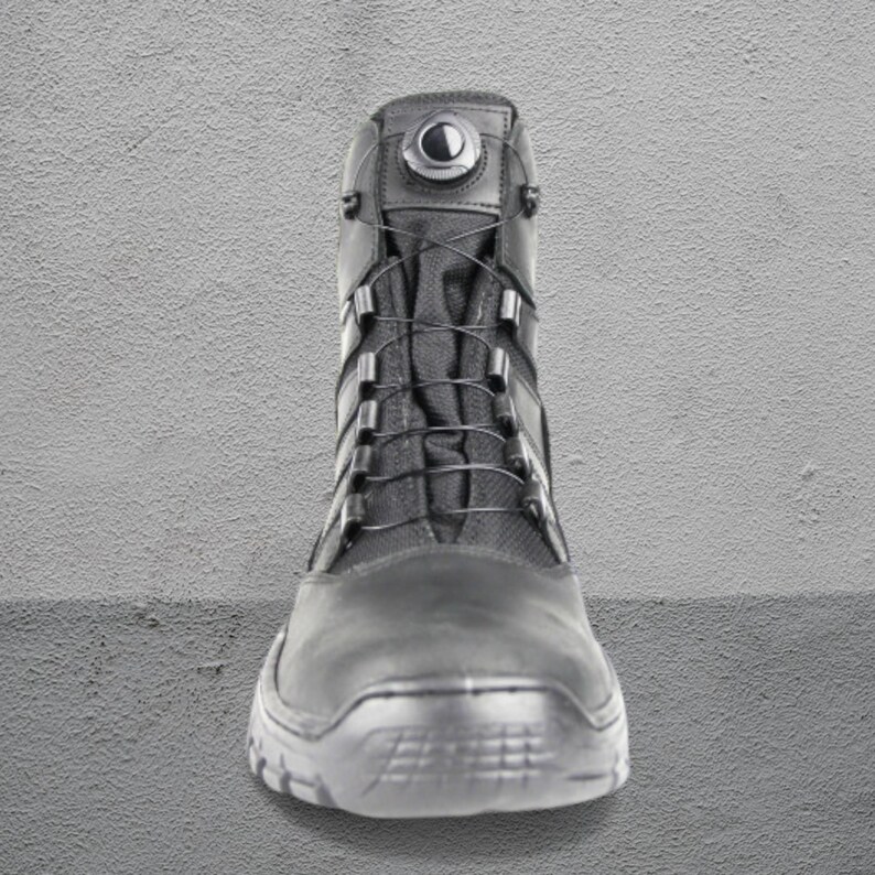 May include: Black tactical boot with a high-top design. The boot features a lace-up closure system with metal eyelets and a round dial at the top. The sole is textured for grip, and the boot is made of durable materials.