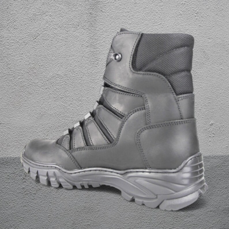 May include: A gray combat boot with a rugged sole and a high-top design. The boot features a lace-up closure, reinforced panels, and a padded collar for ankle support. The boot is made of durable materials.