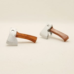May include: Two miniature silver-colored axes with wooden handles. The axes are lying on a white surface.