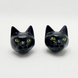 May include: A pair of black cat head earrings with green eyes.
