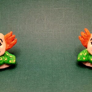 May include: A pair of clown-themed earrings with orange hair, green and white polka dot collars, and red noses.