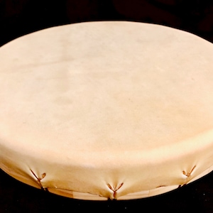 Op de afbeelding: Een ronde, lichtbruine leren trommel met een houten frame. De trommel is strak gespannen en klaar om te bespelen.