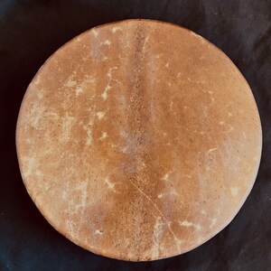 Op de afbeelding: Een bruin leren trommelvel met een natuurlijk, licht getextureerd oppervlak. Het vel is rond en heeft een licht verhoogd midden.
