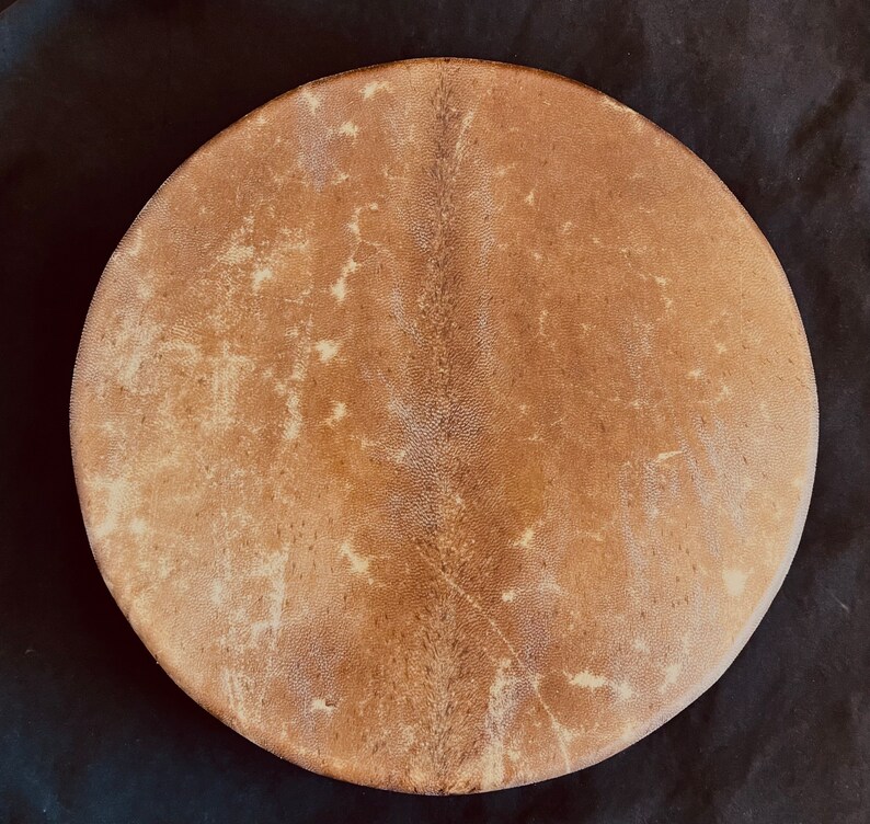 Op de afbeelding: Een bruin leren trommelvel met een natuurlijk, licht getextureerd oppervlak. Het vel is rond en heeft een licht verhoogd midden.