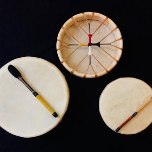 Op de afbeelding: Drie Native American handdrums met houten frames en rauwe huiden. Twee drums hebben houten stokken en &eacute;&eacute;n drum heeft een zwarte en gele stok.