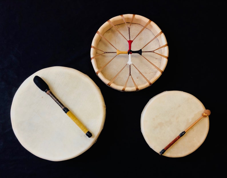 Op de afbeelding: Drie Native American handdrums met houten frames en rauwe huiden. Twee drums hebben houten stokken en &eacute;&eacute;n drum heeft een zwarte en gele stok.
