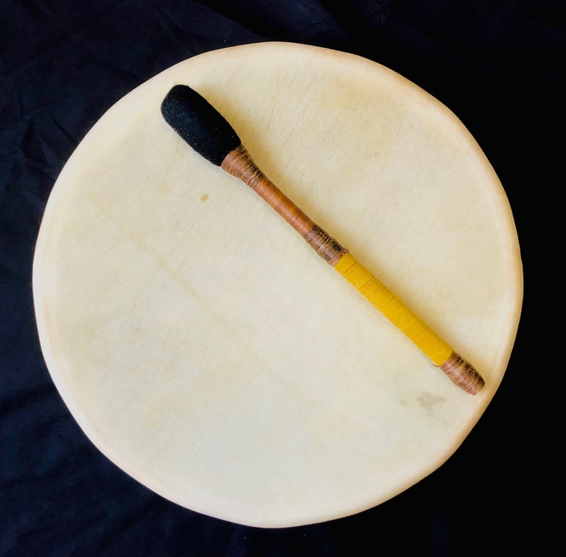 Op de afbeelding: Een witte ronde trommel met een houten beitel met een zwarte, pluche kop en gele en bruine wikkelingen.