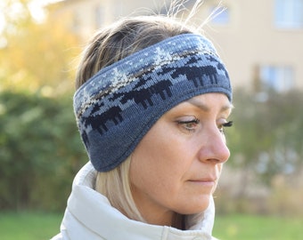 Puede incluir: Una diadema de lana para orejas azul y blanca con un patrón invernal con árboles y alces. La diadema la lleva puesta una persona con el pelo rubio.