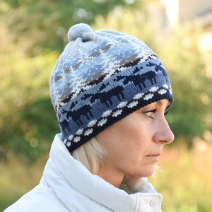 May include: A blue and white knitted hat with a pom pom on top. The hat features a pattern of reindeer and snowflakes.