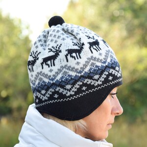 May include: A white and black knit hat with a reindeer pattern and a pom pom on top. The hat has ear flaps that can be tied under the chin.