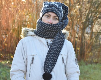 Puede incluir: Una mujer con una chaqueta de invierno blanca con una bufanda y un gorro de patrón blanco y negro. La bufanda tiene un pompón negro en el extremo.
