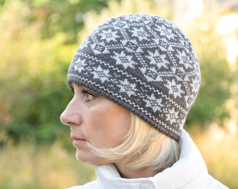 Puede incluir: Un gorro de punto gris y blanco con un patrón geométrico. El gorro lo lleva puesto una persona con el pelo rubio.
