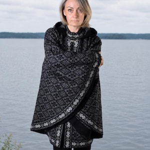 May include: A black and gray hooded cape featuring a repeating geometric star pattern. The garment has a high collar, a front closure with a silver-toned metal clasp, and a solid black interior lining visible along the edges and the hood.