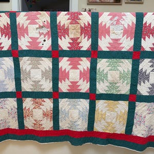 May include: A patchwork quilt featuring a pineapple block pattern in various floral and geometric prints including red, green, blue, yellow, and white. The quilt is divided by dark green sashing and red cornerstones, with a red border and visible wear.