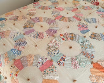 Puede incluir: Un edredón hecho a mano con un diseño floral. El edredón muestra grandes diseños de flores circulares con diversos patrones de tela en colores pastel. Cada centro de flor tiene un pequeño botón marrón. El edredón está sobre una cama.