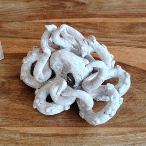 May include: A white ceramic octopus sculpture with a cracked glaze effect. The octopus has multiple curled tentacles and a dark spot for its eye. The sculpture is placed on a wooden surface.