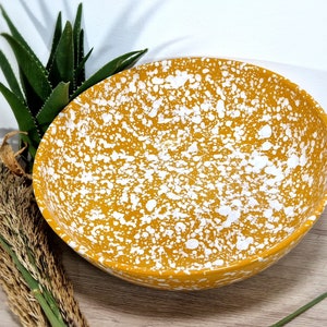 May include: A large, yellow ceramic bowl with white speckles. The bowl is round and has a wide rim.