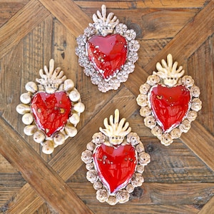 Op de afbeelding: Vier rode keramische harten met witte en gouden accenten. Elk hart is omgeven door een decoratief frame van bloemen en bladeren. De harten worden gepresenteerd op een houten oppervlak.