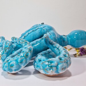 May include: A ceramic octopus sculpture with a blue and green glaze. The octopus has eight tentacles and is lying on its side.